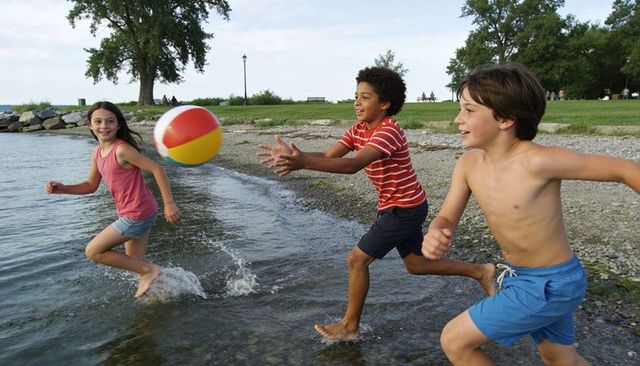 Children running and catching colorful beach ball along lakeshore, splashing summer fun