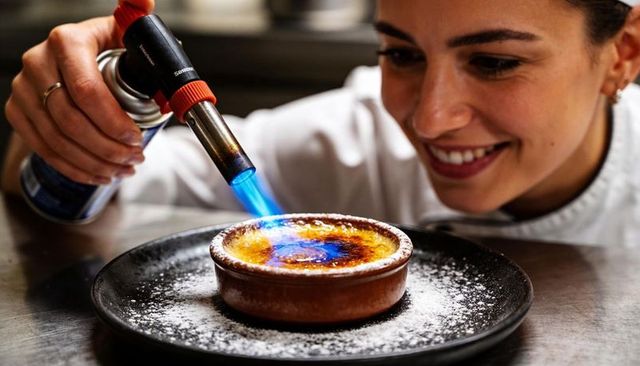 Smiling chef torching crème brûlée with blowtorch, caramelizing sugar in ramekin