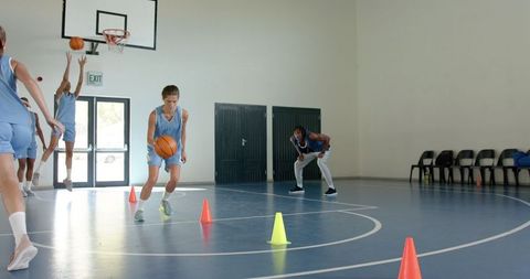 Youthful basketball team practicing with coach in indoor court