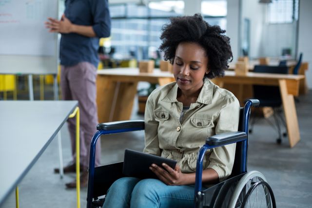 Business executive in wheelchair using digital tablet in modern office. Ideal for promoting workplace diversity, inclusion, and accessibility. Suitable for corporate websites, business presentations, and articles on technology in the workplace.