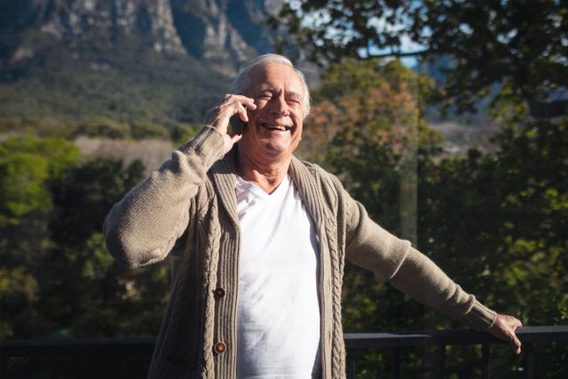 Caucasian senior man smiling while talking on the smartphone in the balcony. retirement senior lifestyle living concept