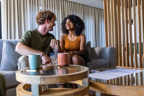 Multiracial couple smiling and chatting on cozy modern living room sofa