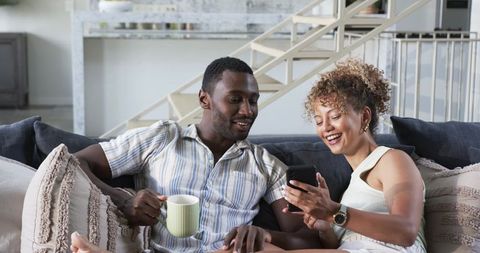 Couple relaxing on couch sharing smartphone and coffee in modern open-plan living room