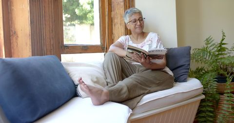 Senior Woman Enjoying Book by Sunlit Window