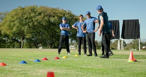 Coach leading youth baseball drills on grassy field with cones, caps, teamwork and focus