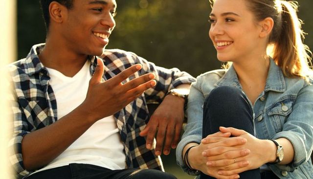 Young friends chatting and laughing on park bench during golden hour outdoor conversation
