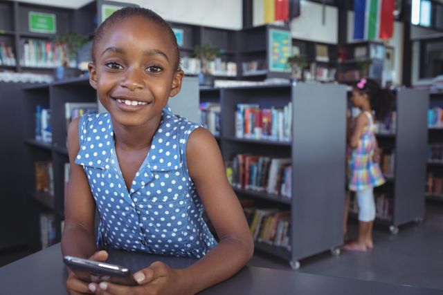 Portrait of smiling girl with mobile phone at desk in library