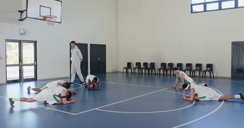 Diverse Basketball Team Stretching with Coach in Gymnasium