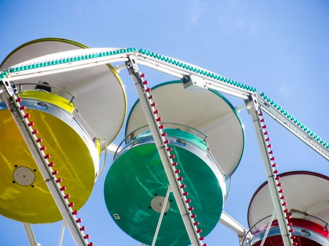 Bright image featuring close-up view of colorful Ferris wheel cabins against clear blue sky. Ideal for themes of amusement parks, festivals, outdoor activities, summer fun, and leisure. Can be used for advertising amusement park events, travel brochures, or social media posts promoting fun activities.