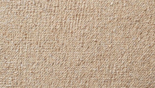 Beige textured plaster surface closeup featuring stucco grain, trowel marks and pitting