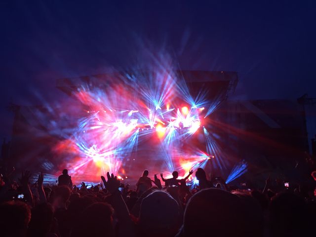 Fans are enjoying a live music concert with colorful stage lights illuminating the night. This can be used for materials related to music festivals, live events, nightlife, entertainment promotions, or concert experiences.