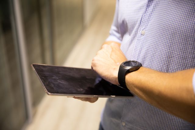 Side view close up of a Caucasian man working in a creative office, holding and using a digital tablet, wearing a blue shirt and a watch on his hand