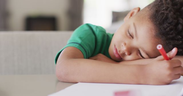 Young child sleeps on a desk while holding a red pen. Perfect for themes of education, childhood fatigue, studying, rest, and academic stress. Ideal for illustrating the importance of sleep, homework challenges, and the balance between studies and rest in young students.