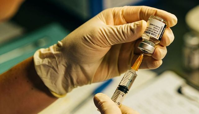 Gloved clinician drawing vaccine from vial into syringe closeup for vaccination shot
