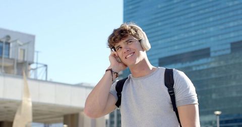 Young man listening to music with headphones and backpack in modern city plaza
