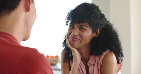 Sunlit kitchen romance: woman wearing pink blouse smiling at partner, cozy candid moment