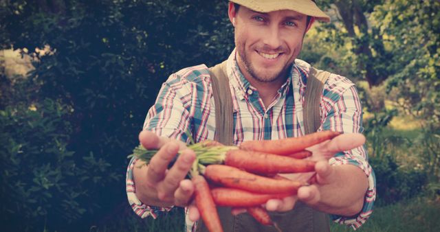 A cheerful farmer is presenting fresh, organic carrots he has just harvested, standing in a lush garden. The image evokes themes of sustainable farming, healthy lifestyles, and happiness with nature. Ideal for articles on sustainable agriculture, advertisements for organic produce, or materials promoting farm-to-table movements.