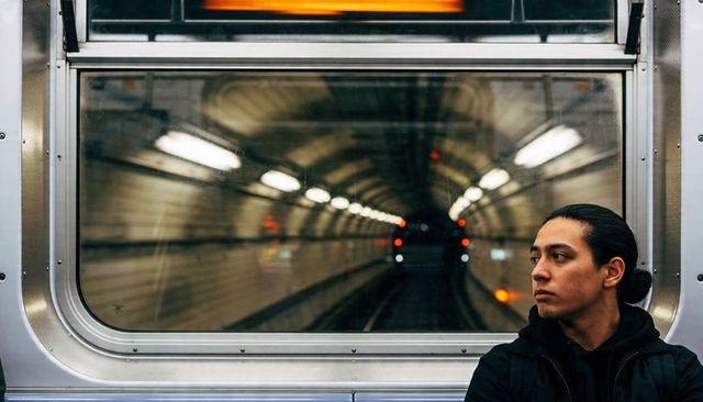 Sitting commuter wearing black hoodie watching tunnel through subway window, moody urban