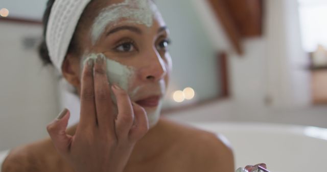 Woman applying a face mask in a cozy, softly lit bathroom. Ideal for illustrating self-care, beauty routines, skincare ads, wellness blogs, and pampering sessions.