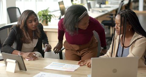 Diverse female colleagues collaborating over analytics charts and laptop at open office