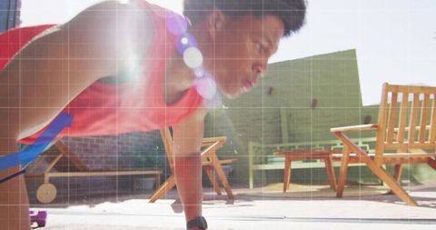 Athletic man performing plank on rooftop terrace with sunlight dumbbell and urban workout