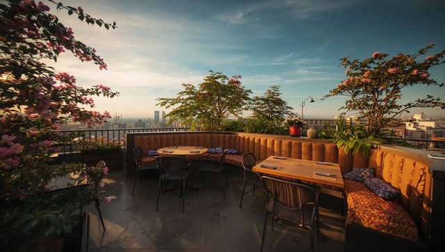 Sunlit rooftop terrace with curved banquette, wooden tables, city skyline at golden hour