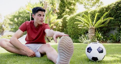 Young Man Stretching Outdoors Next to Soccer Ball for Fitness