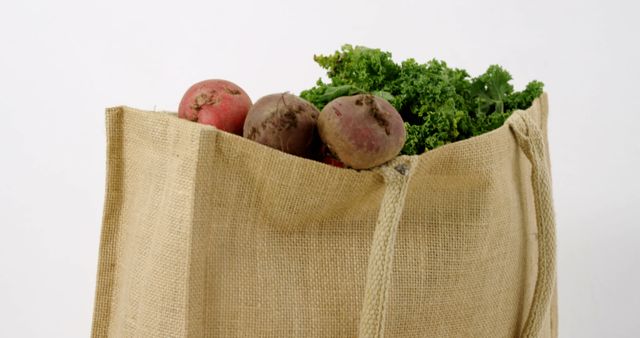 A burlap tote bag is filled with fresh vegetables, including beets and leafy greens, with copy space. Emphasizing sustainability, the reusable bag suggests eco-friendly shopping habits and the importance of consuming fresh produce.