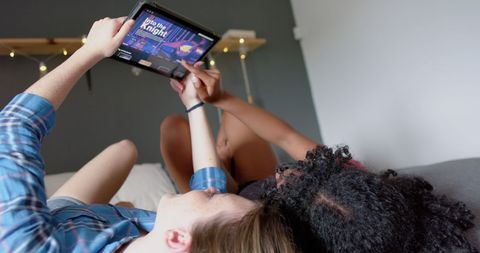 Diverse teenage friends watching movie on tablet in cozy room