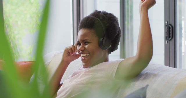 Young woman wearing headphones and smiling while relaxing on a couch. She is enjoying music. Perfect for lifestyle, wellness, home living, and leisure themes.