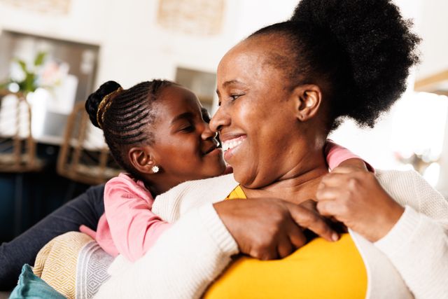 Happy african american granddaughter hugging her smiling grandmother in living room at home. Family, free time and domestic life concept.
