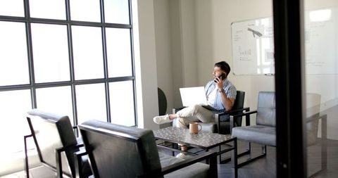 Man engaged in phone call and laptop work in bright office