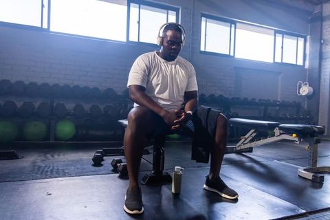 African american man resting after workout on bench in sunlit warehouse gym