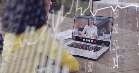 Woman in yellow sweater watching remote business meeting on laptop with financial charts