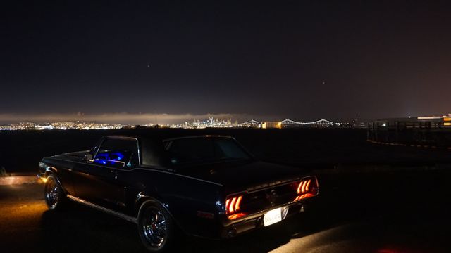 Classic vintage car parked by the waterfront at night with an illuminated city skyline and bridge in the background. Ideal for illustrating urban night scenes, automotive themes, or showcasing scenic city views with a nostalgic touch. Perfect for travel blogs, automotive websites, and content focused on cities and nightlife.