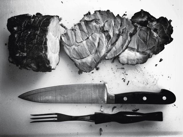 High-quality image of sliced roast beef on a cutting board with a knife and fork. Ideal for use in cooking blogs, culinary websites, food magazines, and restaurant menus. The black and white tones add an artistic feel, making it suitable for both modern and rustic food presentations.