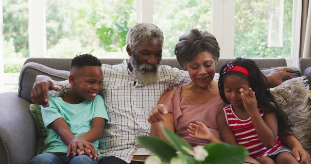 Senior biracial couple sitting on a couch with their grandchildren - Download Free Stock Photos Pikwizard.com