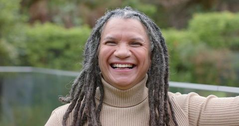Laughing mature woman with dreadlocks wearing beige turtleneck outdoors smiling portrait