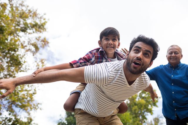 Smiling grandfather looking at man giving piggy backing to son with arms oustretched in yard