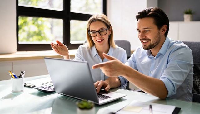 Young professionals collaborating at laptop in bright modern office smiling and pointing