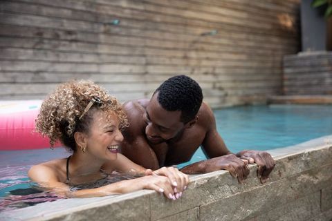Couple laughing leaning on stone pool edge enjoying backyard summer romance