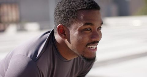 African American athlete leaning on bleachers smiling after workout in outdoor stadium