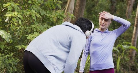 Friends pausing and catching breath on sunlit forest trail during outdoor run