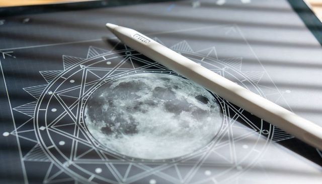 White stylus lying on tablet displaying moon mandala with pattern and blind shadows