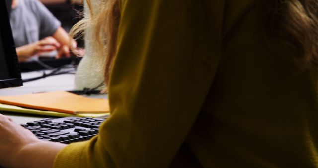 Close up of blonde woman typing on computer keyboard in modern office environment. Ideal for content related to workplace scenarios, business technology, and professional activities.