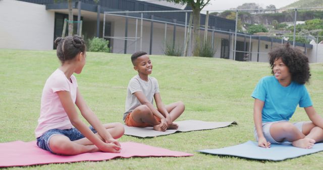 Three kids sitting on yoga mats on a grassy field, smiling and chatting, enjoying outdoor relaxation and summer weather. Perfect for illustrations related to healthy lifestyles, childhood fitness, exercise programs for kids, and outdoor activities.