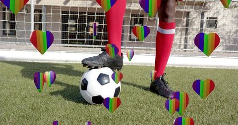 Soccer player balancing ball at goal with rainbow hearts celebrating pride