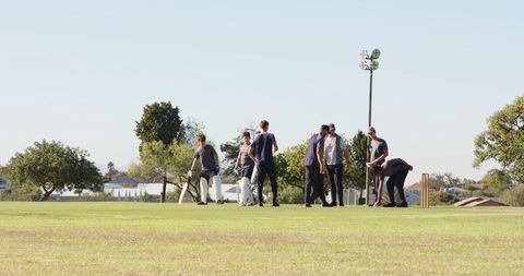 Cricket team walking toward wicket, huddling and cheering before match on sunny field
