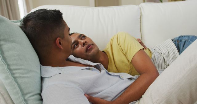 Smiling biracial gay male couple hugging lying on sofa together. staying at home in isolation during quarantine lockdown.