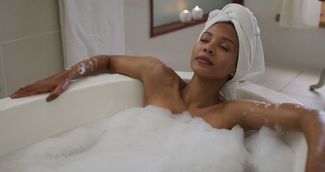 Young woman enjoying a relaxing bath with bubbles. With candles lit in the background, it creates a calm and serene atmosphere. Ideal for concepts related to self-care, relaxation, spa treatments, personal well-being, and at-home beauty routines.